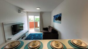 En moderne stue med et fladskærms-TV, en sofa og et spiseområde med et bord dækket til to.