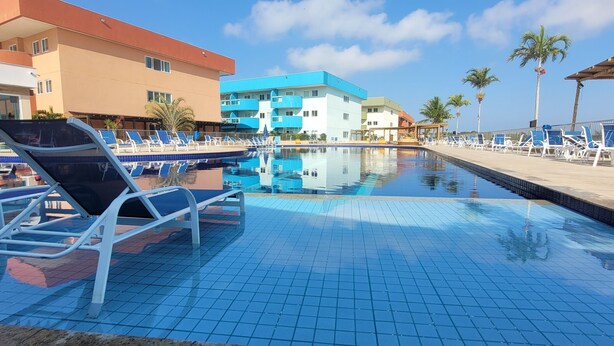 En swimmingpool med liggestole, en palme og en bygning med balkoner.