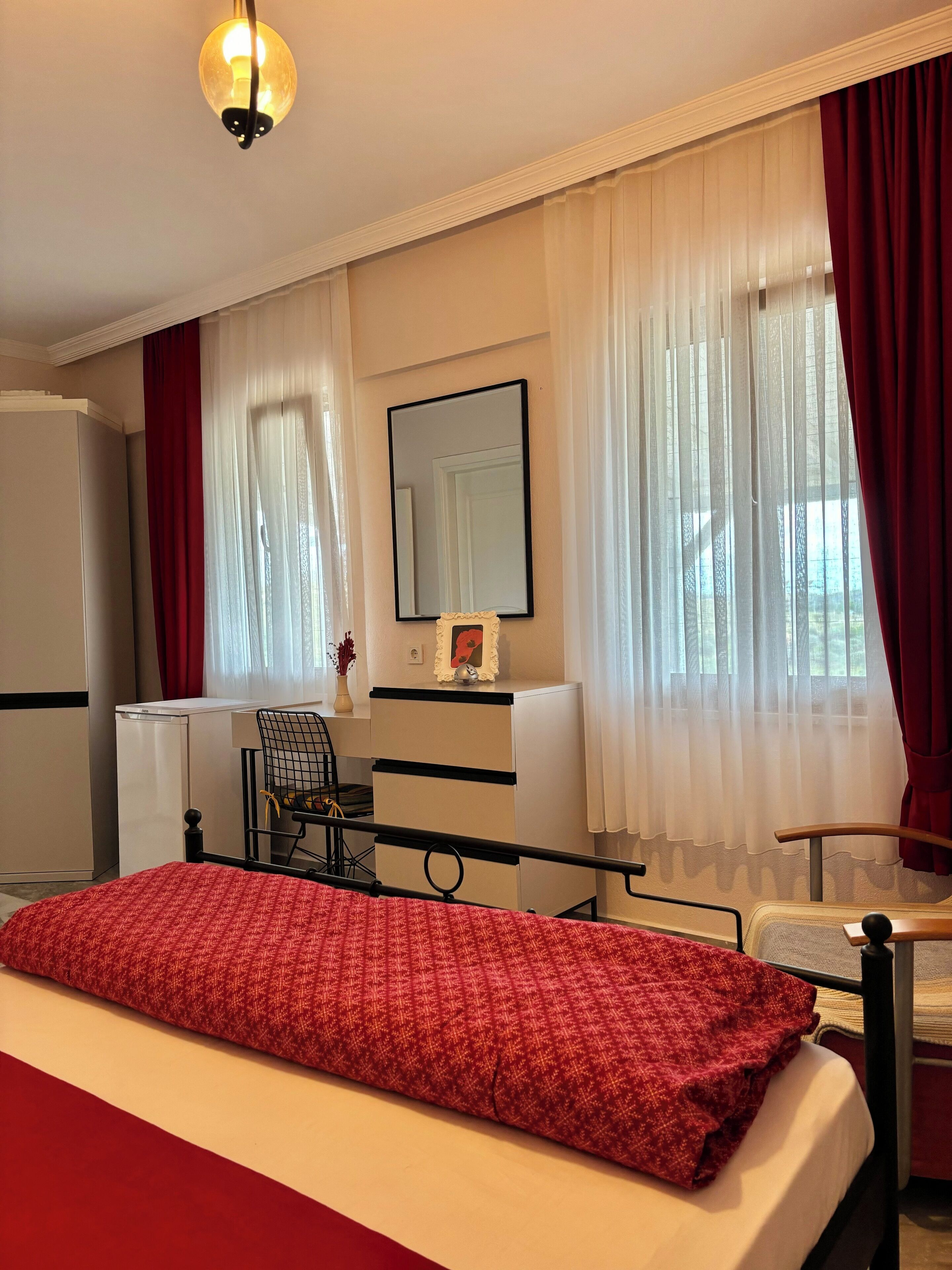 A hotel room with a bed, a desk, a chair, a mirror, and a window with curtains.