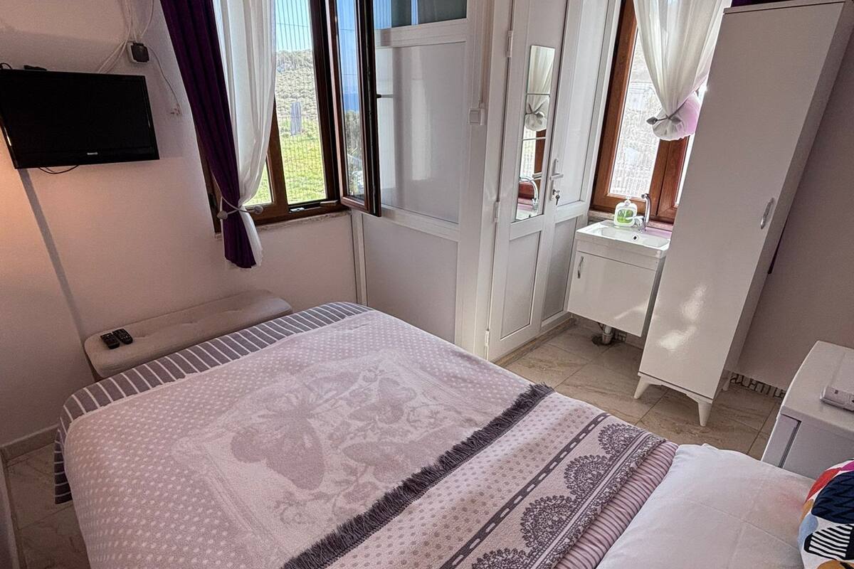 Une chambre à coucher comprenant un lit, un téléviseur fixé au mur, une armoire, un miroir et une fenêtre avec des rideaux.