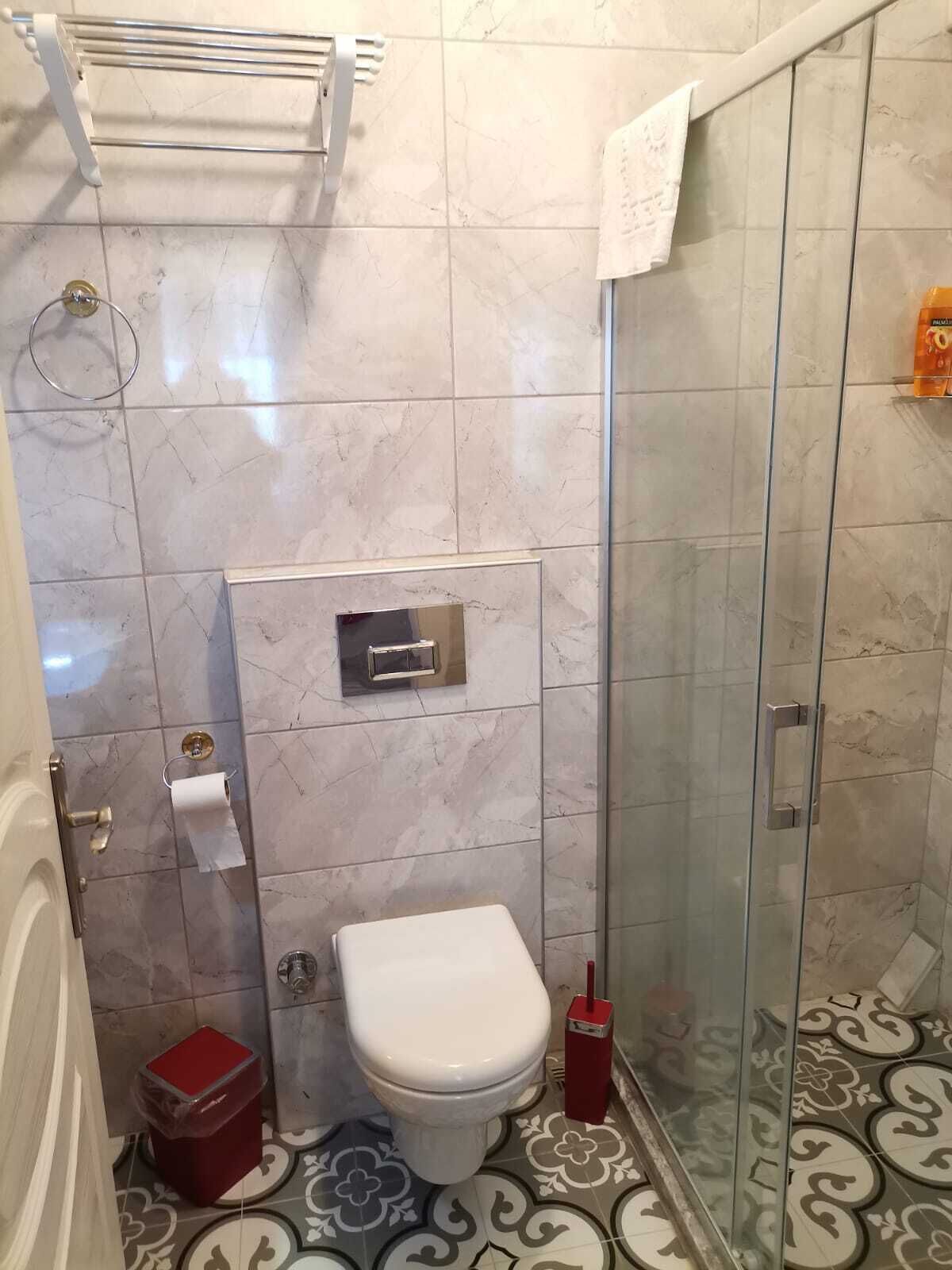 A bathroom with a toilet, a glass shower enclosure, and a marble-tiled floor.