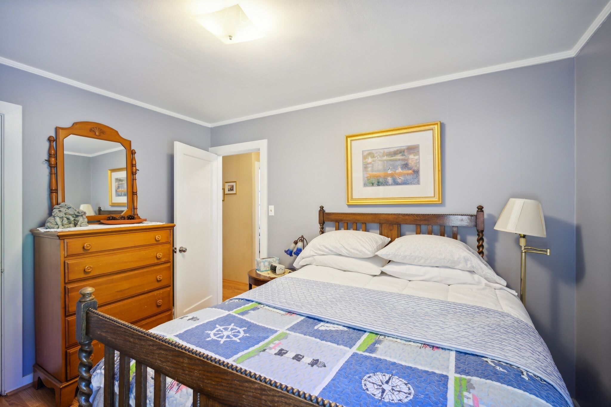 A bedroom with a wooden bed, a dresser, a nightstand, a framed picture on the wall, and a lamp.