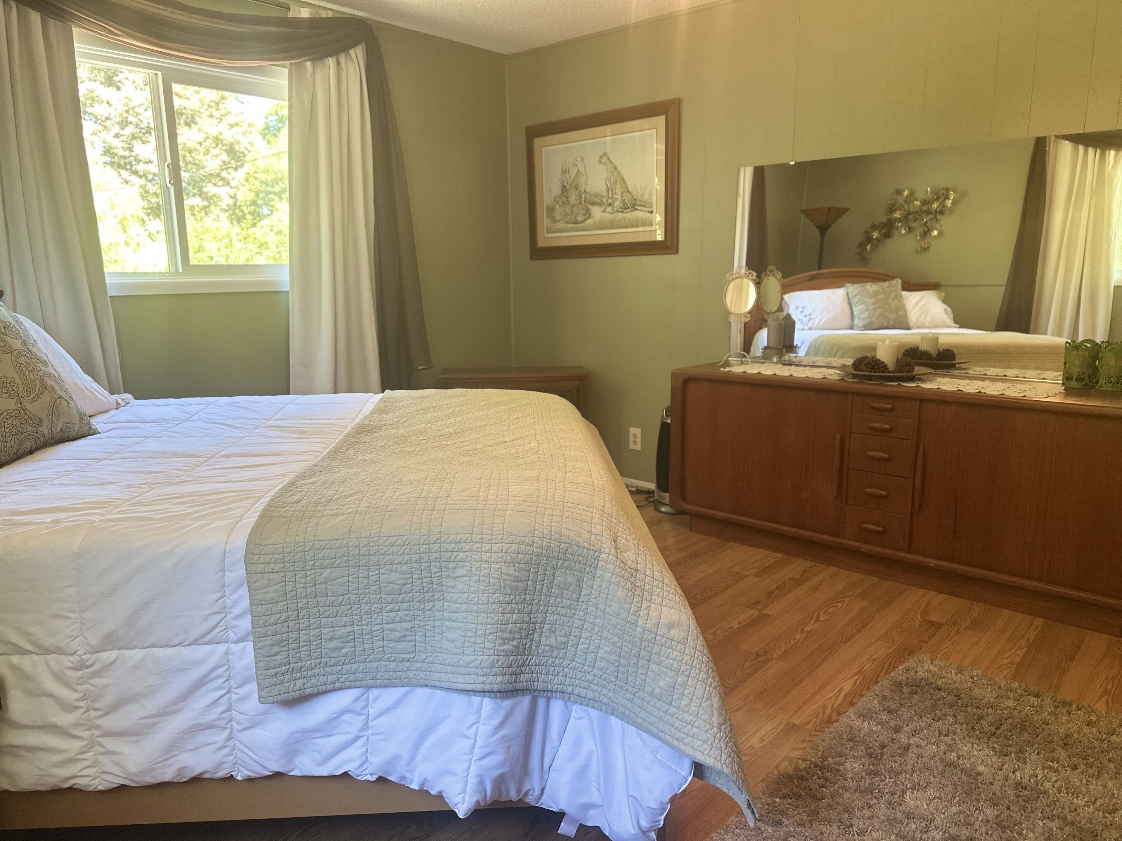 A bedroom with a large bed, a dresser, a mirror, and a framed picture on the wall.