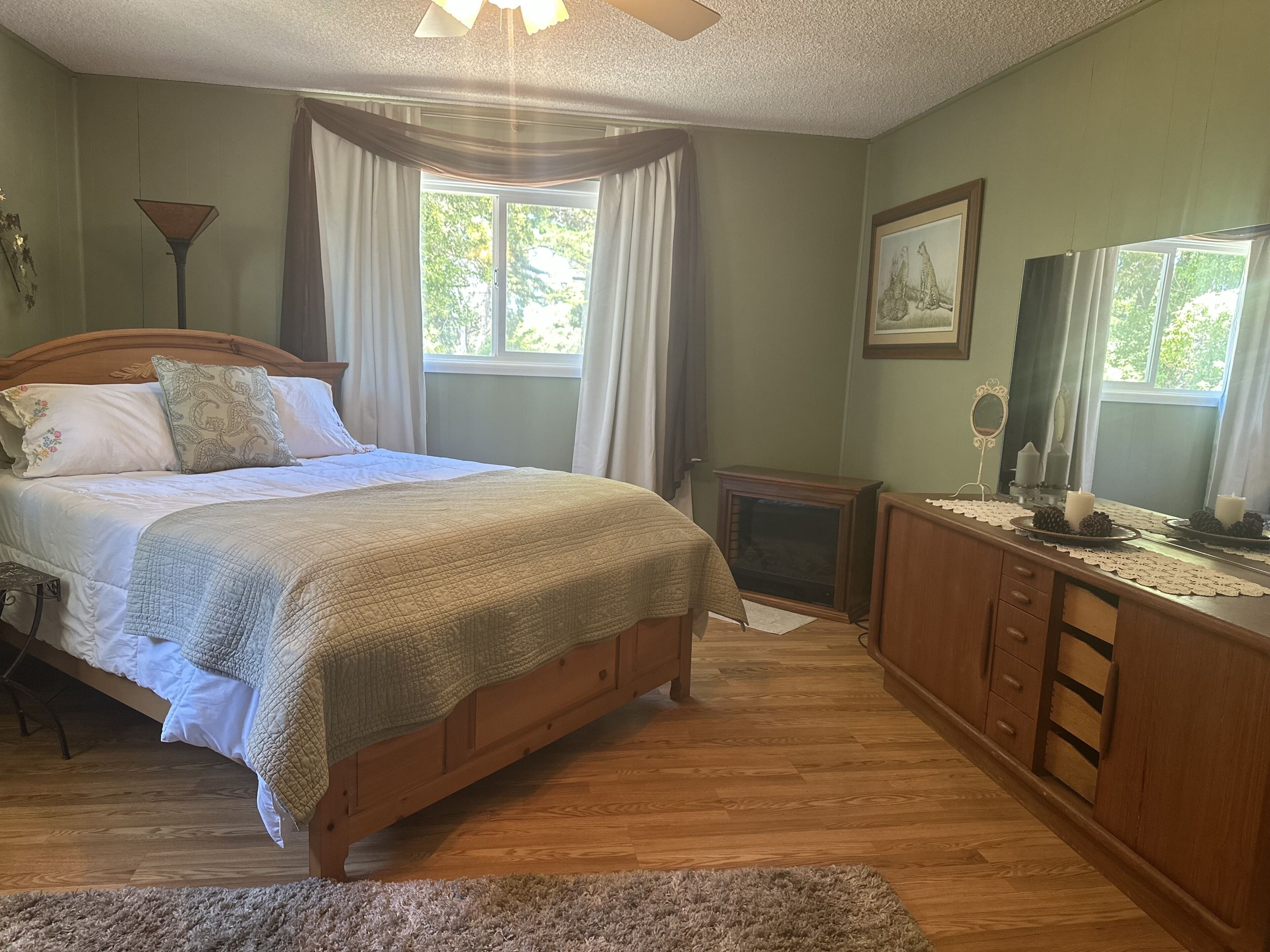 A bedroom with a wooden bed, a dresser, a mirror, and a window with curtains.
