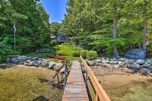 A wooden dock leading to a house surrounded by lush greenery and a clear water body.