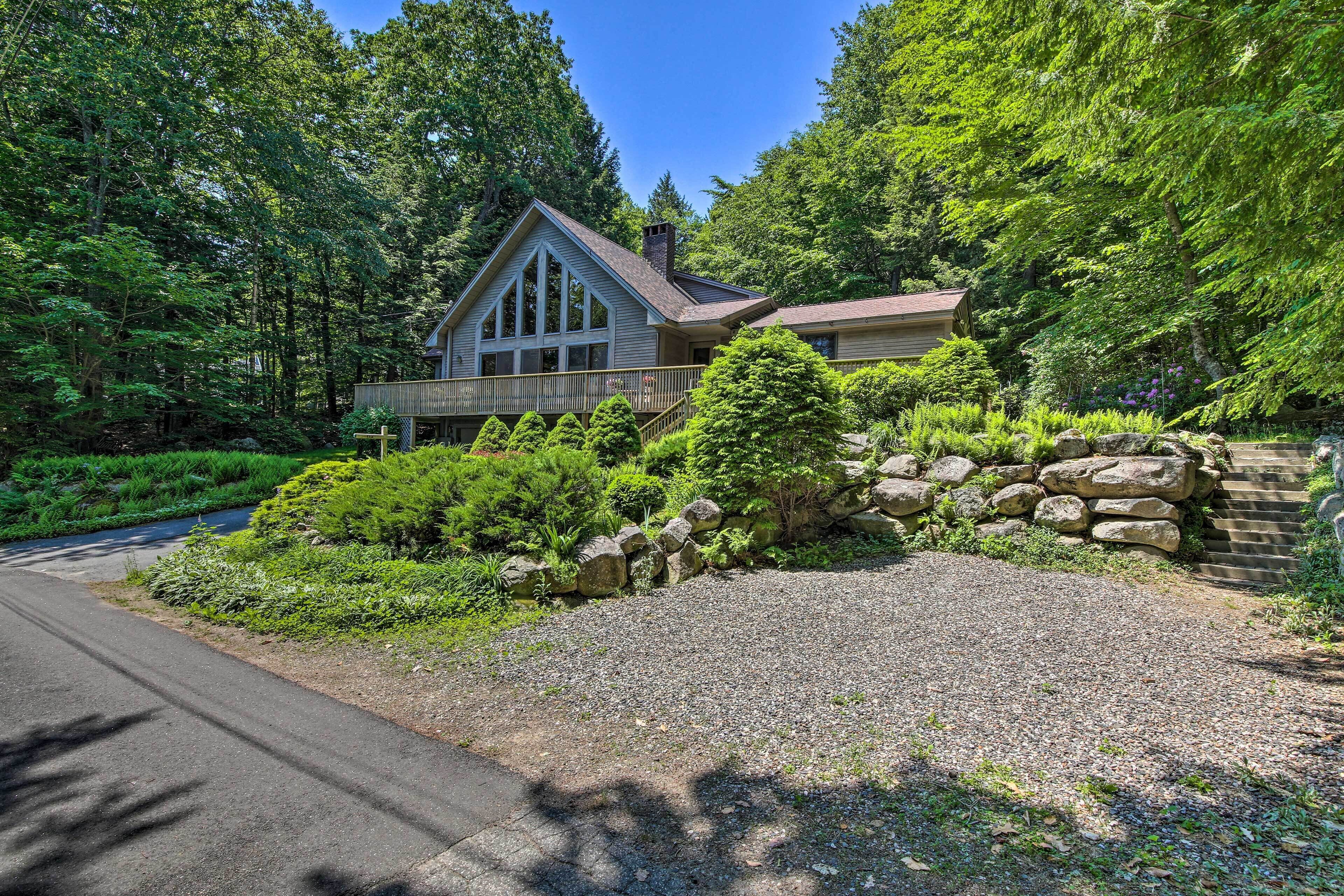A house with a stone retaining wall, surrounded by lush greenery and trees.