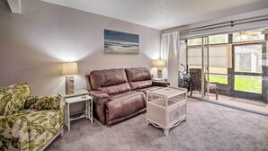 A living room with a brown leather sofa, a floral armchair, a small table, and a glass door leading to a patio.