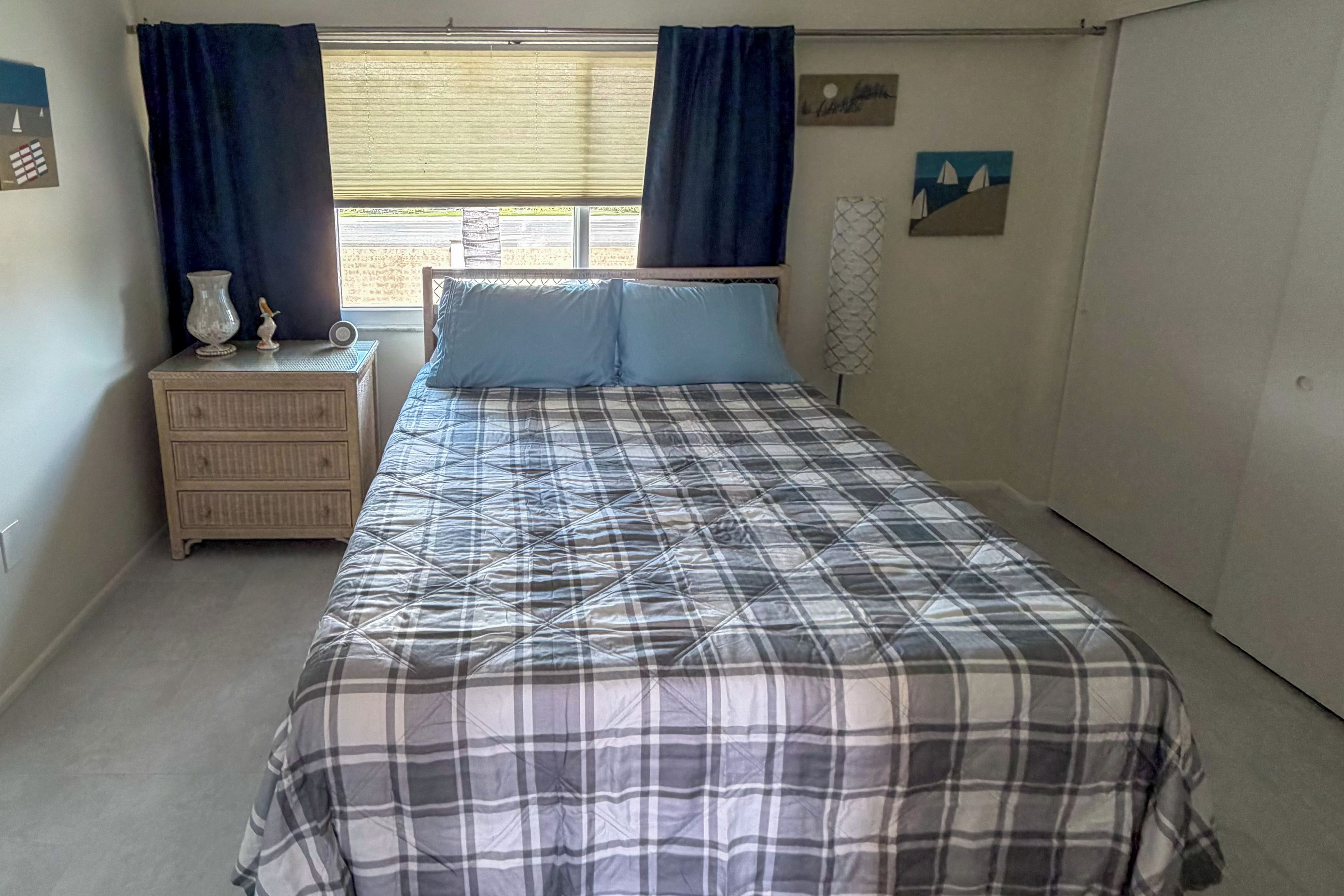 A bedroom with a bed, a nightstand, a dresser, a window with curtains, and a wall with a picture.