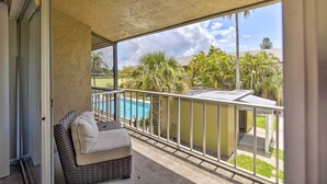 A balcony with a wicker sofa and a view of a swimming pool.