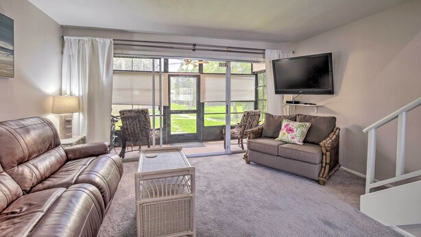 A living room with a brown leather couch, a grey sofa, a wicker coffee table, and a flat-screen TV mounted on the wall.