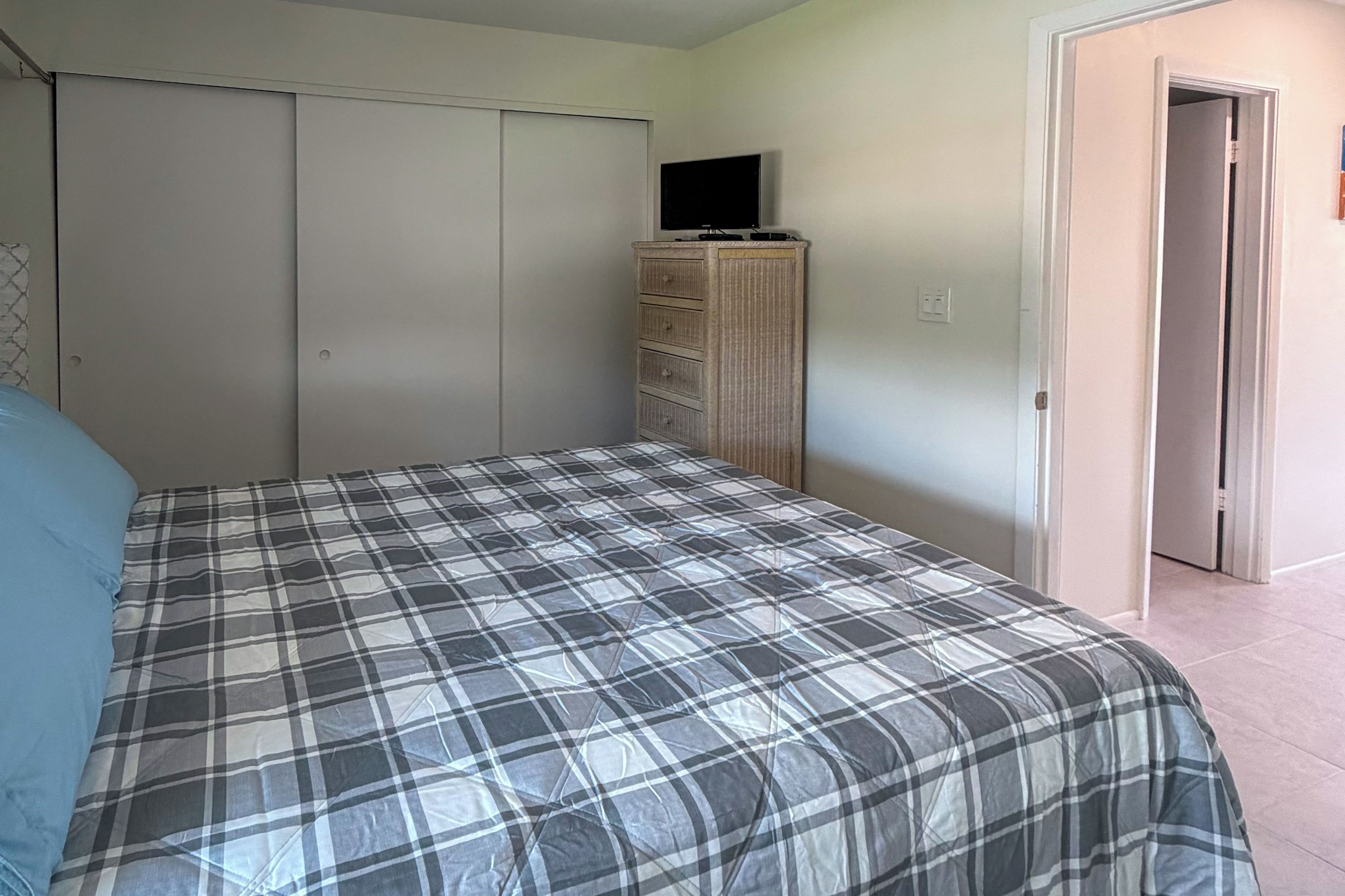 A bedroom with a bed, a wardrobe, a television on top, and a door leading to another room.