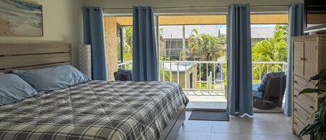 A bedroom with a bed, curtains, a ceiling fan, and a view of the outside.
