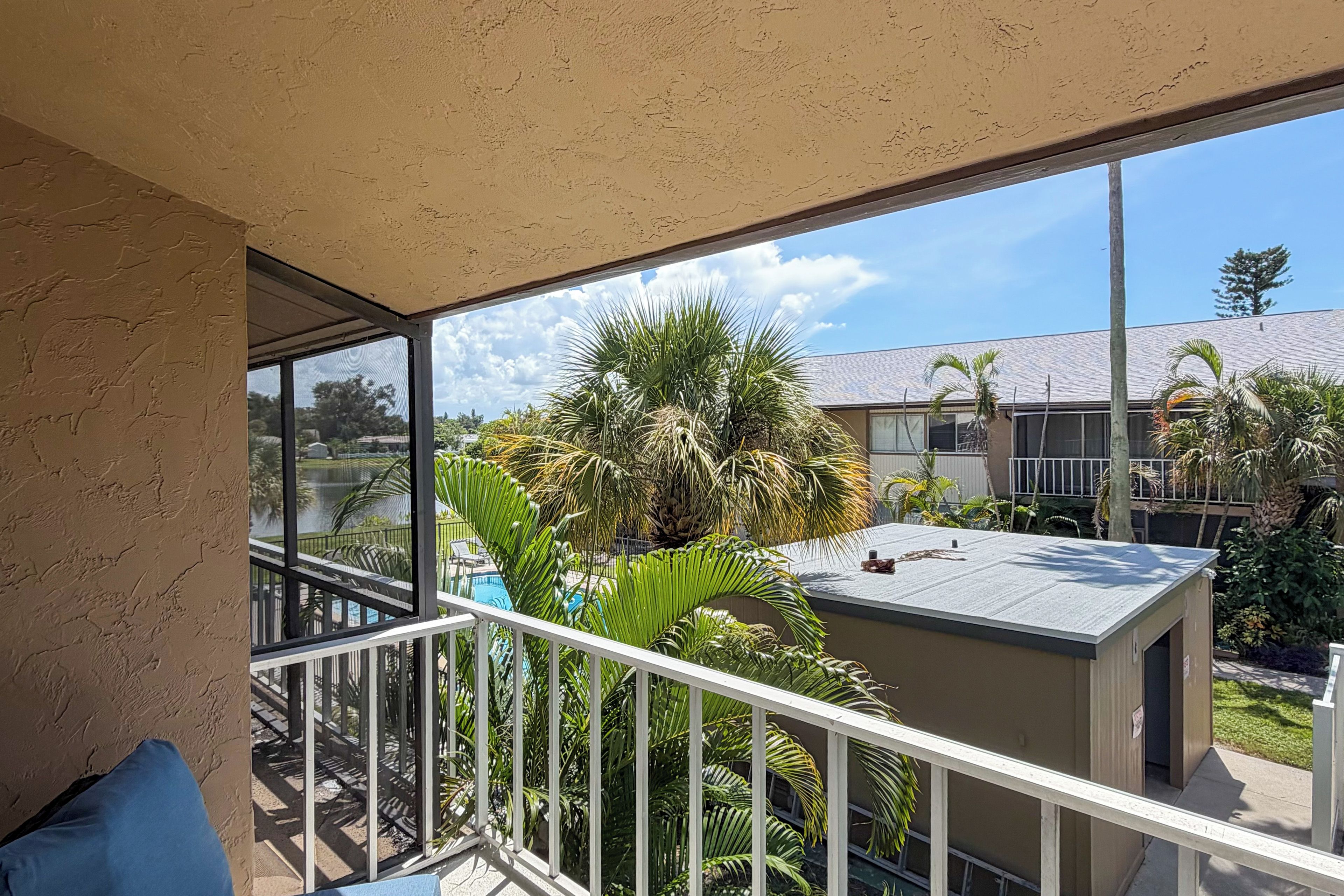 A balcony with a view of a pool, palm trees, and a building with a tiled roof.