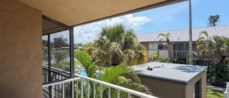 A balcony with a view of a pool, palm trees, and a building with a tiled roof.