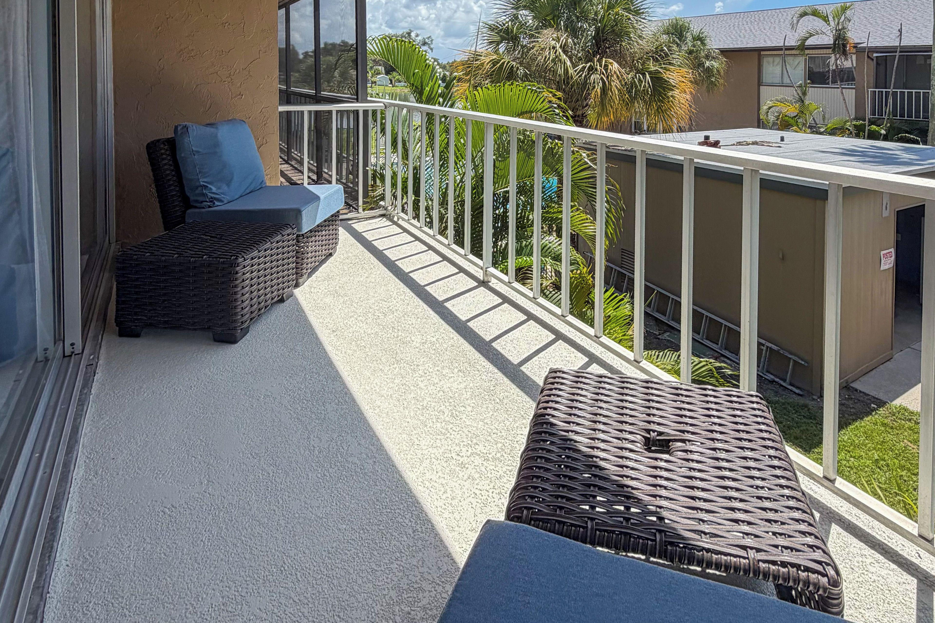 A balcony with wicker furniture, a view of palm trees, and a building in the background.