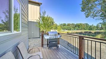 A deck with a grill, chairs, and a view of a natural landscape.