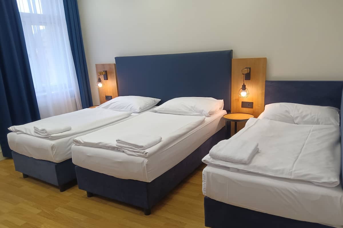 A hotel room with two single beds and a larger bed, all neatly made with white linens.