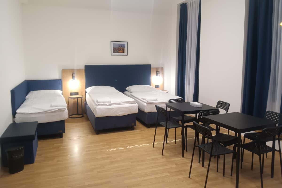 A hotel room with two single beds, a small table with chairs, a trash bin, and a picture on the wall.