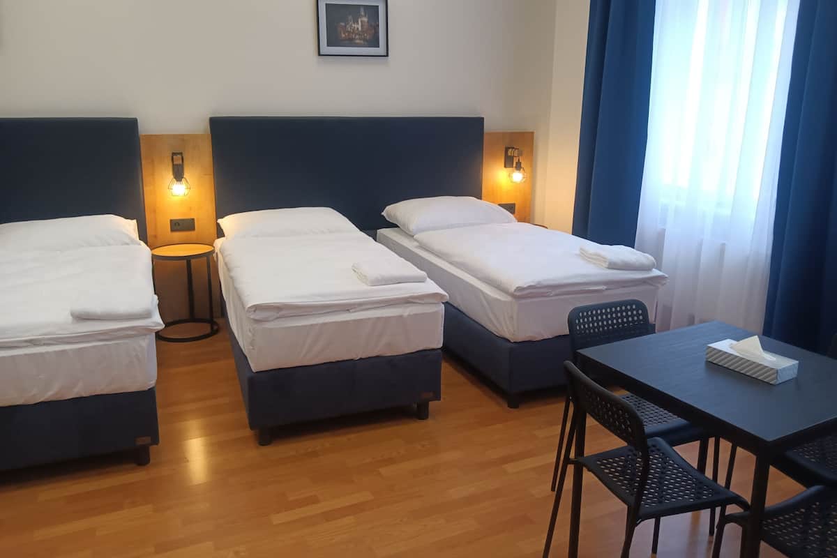 A hotel room with two single beds, a small table with a chair, and a picture on the wall.