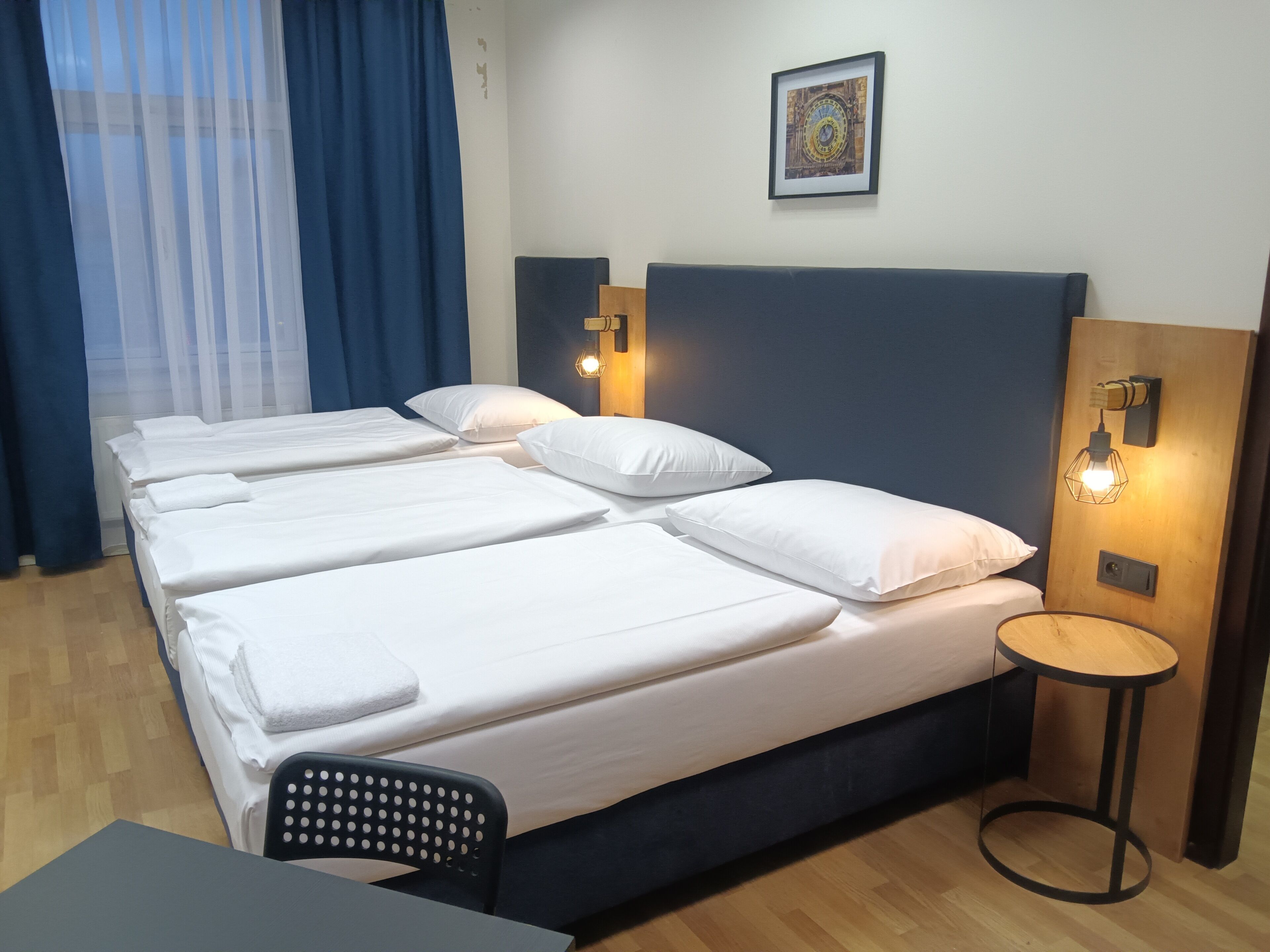 A hotel room with a large bed, two bedside tables, a small round table, a chair, and a wall-mounted clock.