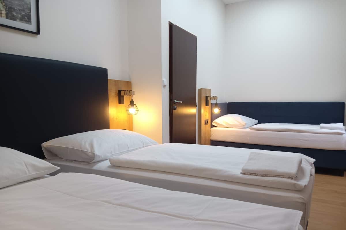 A hotel room with two single beds, a dark headboard, a wooden door, and wall-mounted lights.