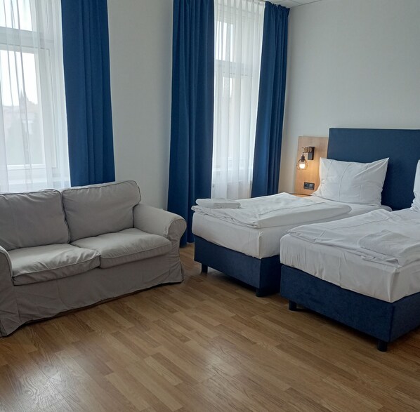 A hotel room with a grey sofa, two single beds, and a wooden floor. - Powder Tower Suites (Prague)