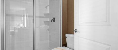A bathroom with a glass-enclosed shower, a toilet, and a white door.