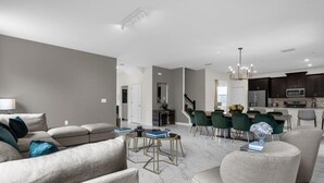 A modern living room with a sofa set, a dining area with chairs, and a kitchen with dark cabinets and appliances. - 7 Bedrooms Storey Lake Resort Home (Kissimmee)