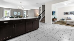 A modern kitchen with dark cabinetry, a large island, and a staircase leading to a living area with a sofa and a coffee table. - 7 Bedrooms Storey Lake Resort Home (Kissimmee)