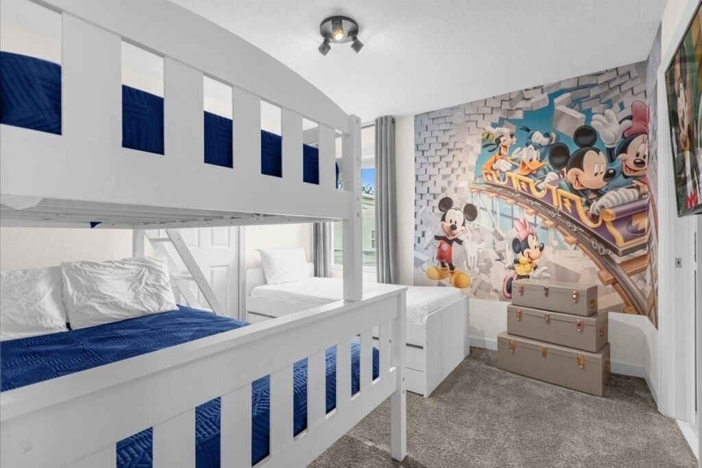 A child's room with bunk beds, a Mickey Mouse mural, and a desk.