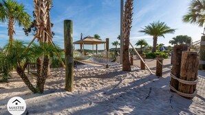 A sandy beach area with palm trees, a hammock, and a wooden structure. - 9 Bedrooms S / Storey Lake Home by RedAwning (Kissimmee)