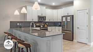 A modern kitchen with white cabinets, stainless steel appliances, a large island with bar stools, and pendant lighting. - 9 Bedrooms S / Storey Lake Home by RedAwning (Kissimmee)