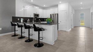 Een moderne keuken met witte kasten, een centraal kookeiland met barstoelen, een roestvrijstalen koelkast en een magnetron.