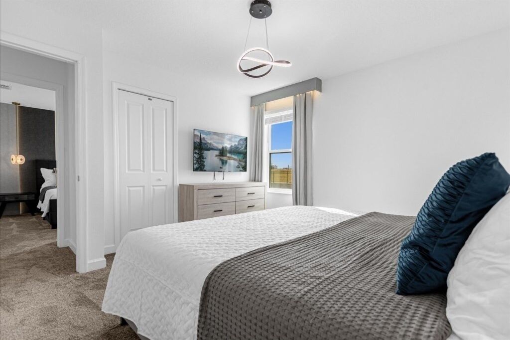 A bedroom with a large bed, a dresser, a TV, and a window with a view.