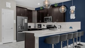 Une cuisine moderne avec des meubles de couleur sombre, un réfrigérateur en acier inoxydable, un four à micro-ondes et un grand îlot central doté de tabourets de bar.