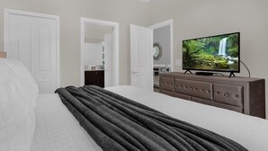 Une chambre à coucher avec un lit, un téléviseur posé sur une commode et une porte donnant sur une autre pièce.