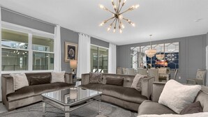 Un salon moderne avec un canapé d’angle, une table basse en verre et un lustre.