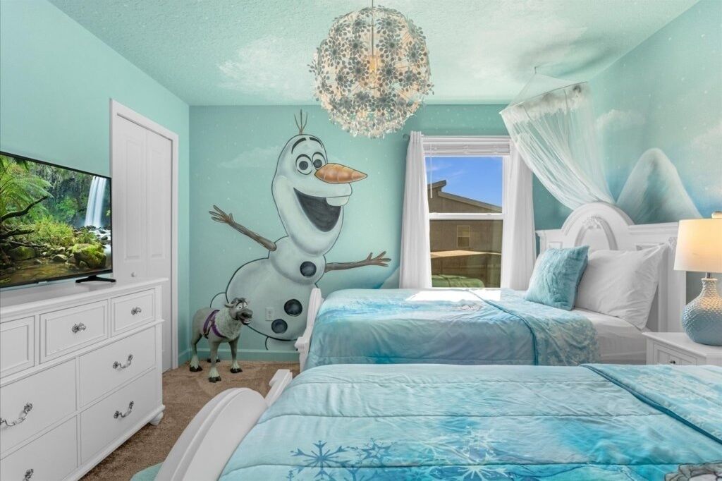 A bedroom with a mural of a snowman, a TV, a dresser, two beds, and a chandelier.