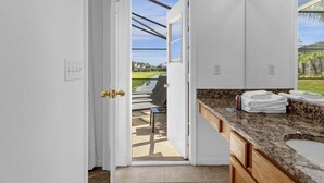 A bathroom with a granite countertop, a sink, and a view of a patio with a chair and a table.