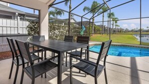 An outdoor patio with a pool, a table with chairs, and a view of a lake and palm trees.