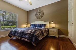 Ein Schlafzimmer mit einem Bett, Nachttischen, einer Wanduhr und einem Fenster mit Jalousien.