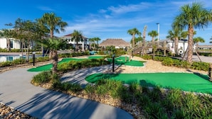 Een golfbaan met een putting green, palmbomen en een zwembad op de achtergrond.