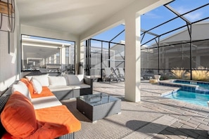 A modern outdoor living area with a sofa, chairs, a glass coffee table, and a pool.