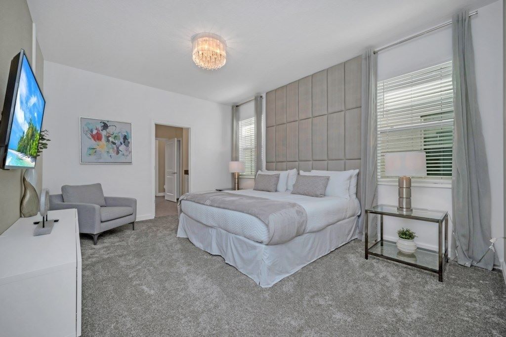 Un dormitorio moderno con una cama grande, un televisor, un escritorio y una ventana con persianas.