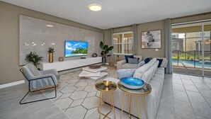 Una sala de estar moderna con un televisor grande, asientos cómodos, una mesita de centro y vista a una piscina.