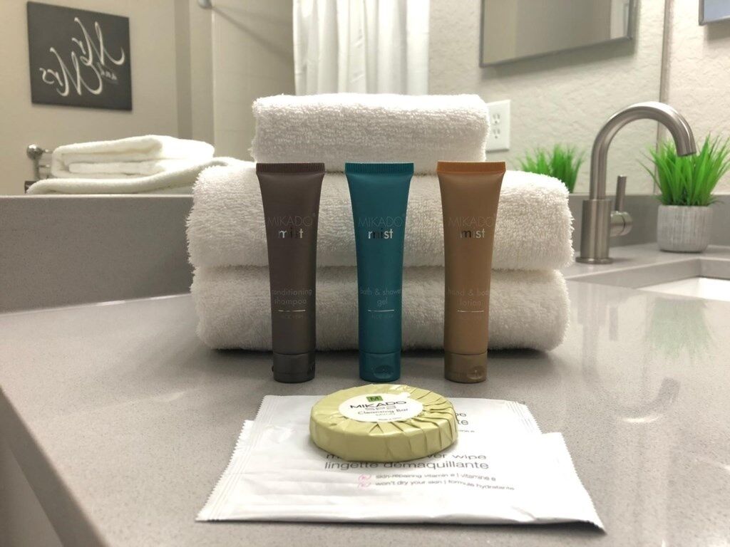 Ein Badezimmer mit Waschbecken, Spiegel und Pflegeprodukten, darunter drei Shampooflaschen und eine Seife.