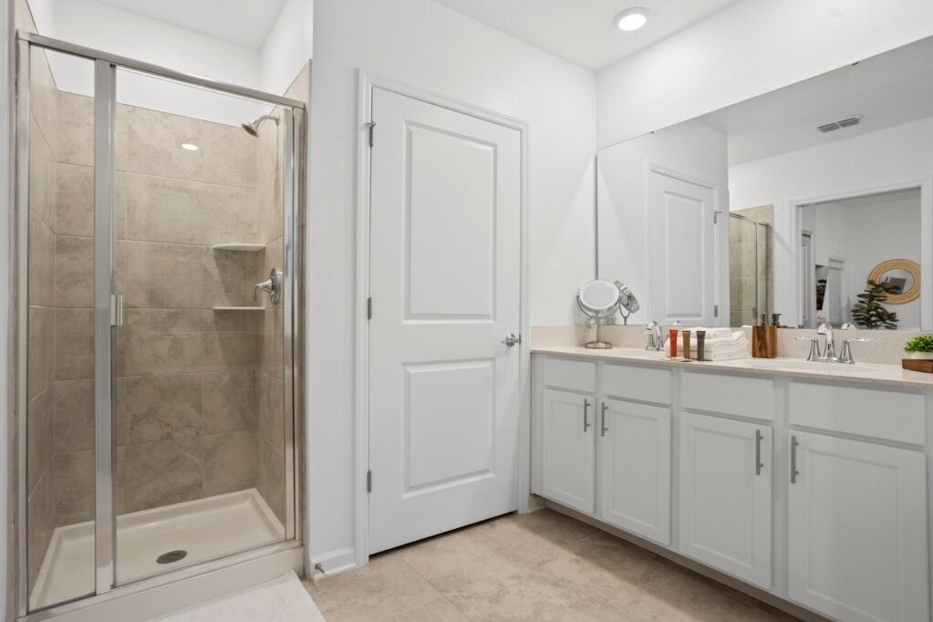 A modern bathroom with a glass shower enclosure, white cabinetry, and a large mirror.