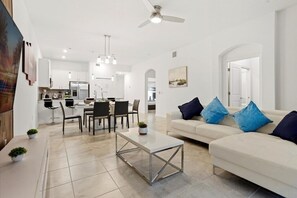 Ein modernes Wohnzimmer mit einem weißen Sofa, einem Couchtisch und einem Essbereich mit Stühlen und einem Tisch.