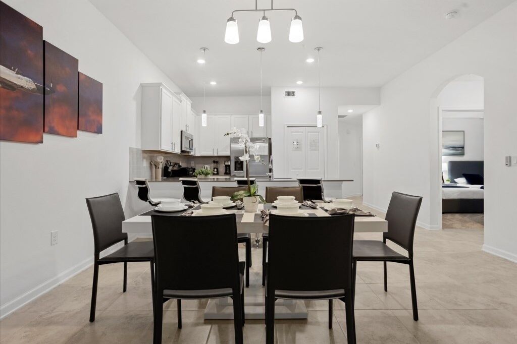 Un espace de salle à manger moderne avec une table centrale, des chaises noires et des luminaires suspendus.