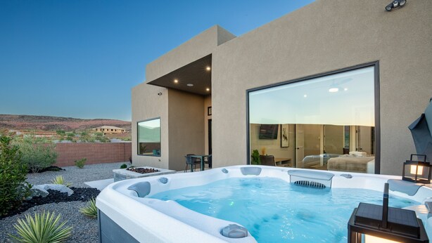 A modern outdoor hot tub area with a clear view of the surrounding landscape, a large sliding glass door leading to a living area, and a patio with seating.